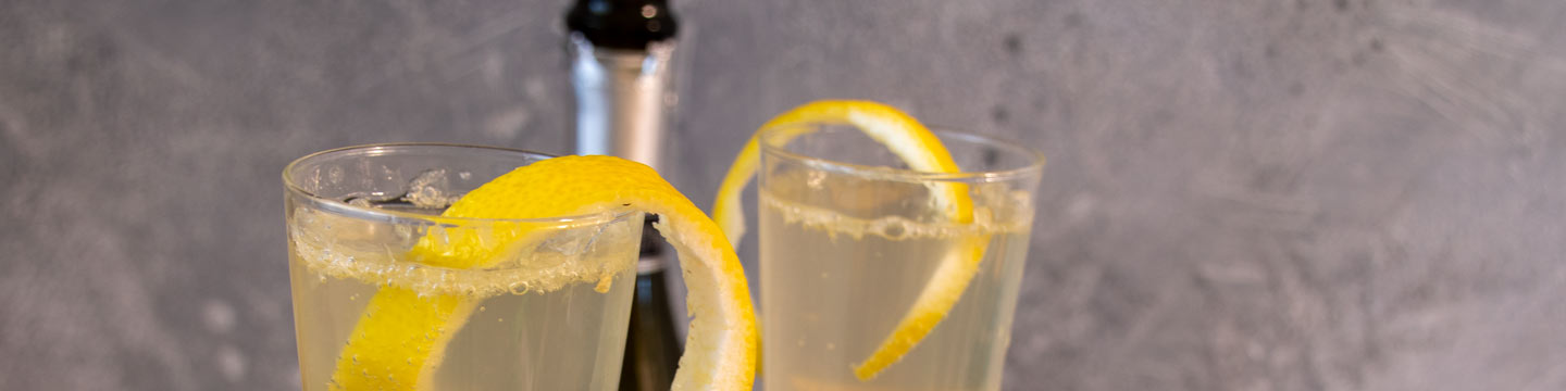 Two french 75 cocktails garnished with lemon peels, with a sparkling wine bottle in the background.